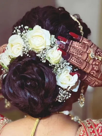 A close up of the bride's hands as she adjusts her floral hair bun. The intricate back hand mehendi looks beautiful against her traditional attire.