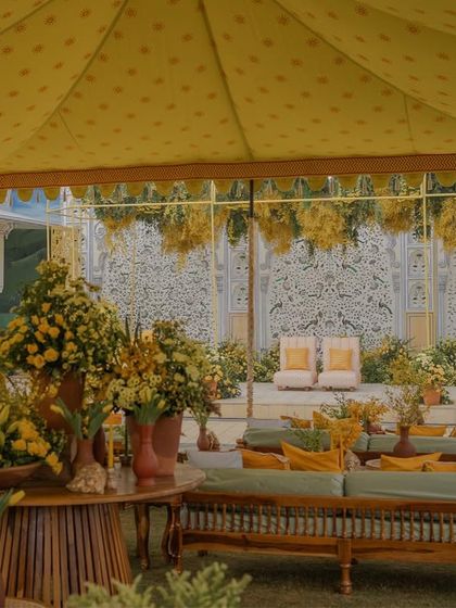 A large seating area under a yellow tent, with a beautiful hand-painted wall serving as a backdrop for the Haldi ceremony.