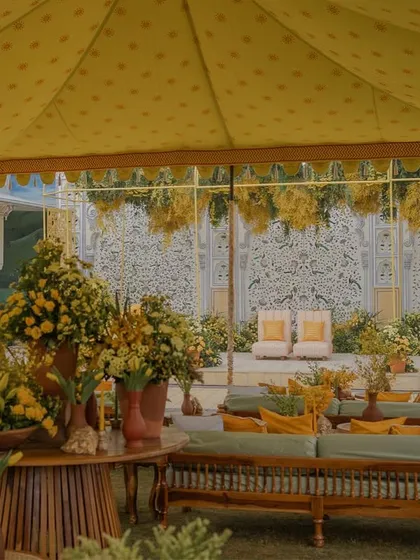 A large seating area under a yellow tent, with a beautiful hand-painted wall serving as a backdrop for the Haldi ceremony.
