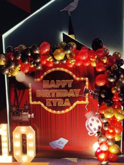 Lights, camera, action. This movie-themed 10th birthday party for Kyra featured a red curtain backdrop, a custom marquee sign, and a black, red, and gold balloon arch to give it a real Hollywood premiere feel.