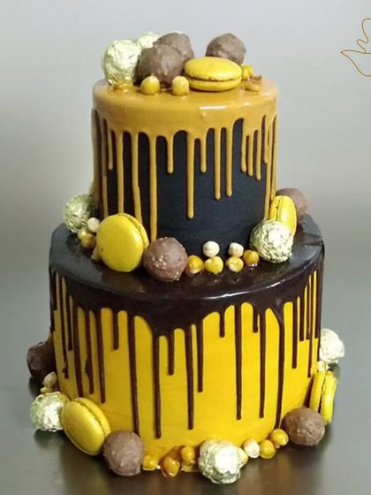 A bold and beautiful two-tier drip cake in black and yellow, adorned with macarons and Ferrero Rocher. A stunning choice for a grand celebration.