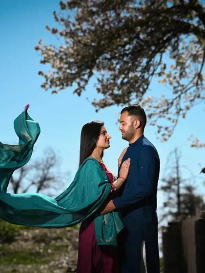 A playful and romantic shot where the bride's dupatta flies in the wind, creating a beautiful, dynamic shape against the clear blue sky. This is a perfect example of capturing movement and emotion.