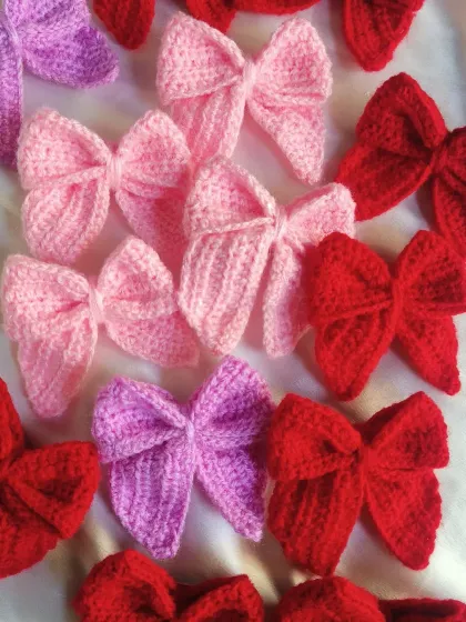 Bow stacking! A lovely pile of our handmade crochet Sailor Bows in shades of red, pink, and purple.