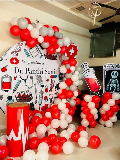 A unique doctor-themed party to celebrate a new graduate. The setup includes a custom backdrop with medical illustrations, red and white balloons, and fun props like an X-ray and syringe cutout.