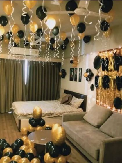 A stylish black and gold themed room decoration for a birthday, with a foil curtain backdrop and balloons filling the space.