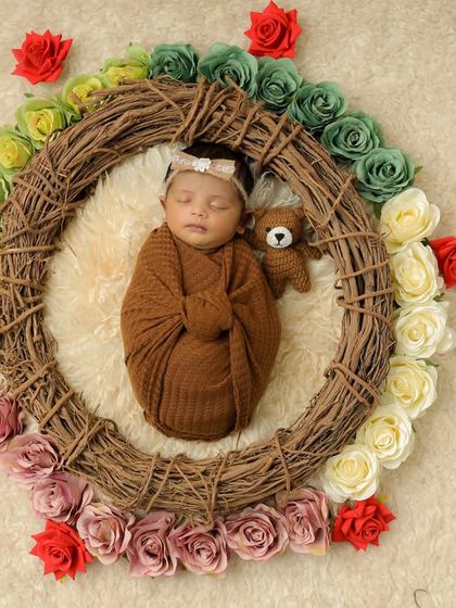 This newborn is sleeping soundly while holding a small teddy bear, framed by a beautiful wreath of roses. Our team is skilled at posing babies safely to get these adorable shots.