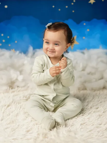 A happy, clapping baby against the dreamy cloud and star background. Her joy is infectious, making for a heartwarming portrait.