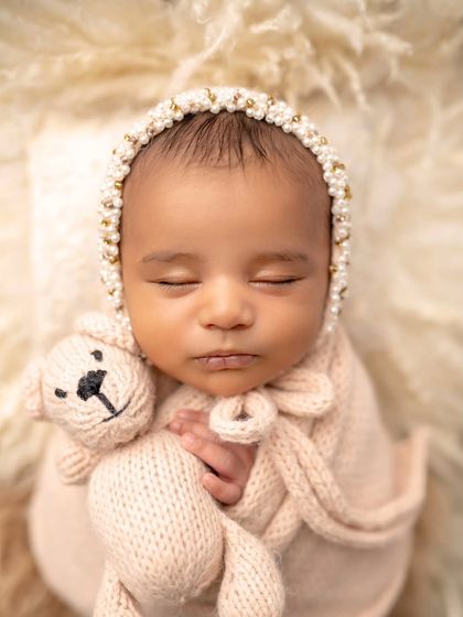 A close-up of a newborn princess holding her tiny teddy bear. The details on the bonnet and the soft textures are beautiful.
