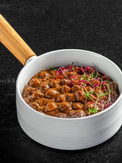A rich and dark mushroom curry, presented in a contemporary white bowl with a wooden handle.