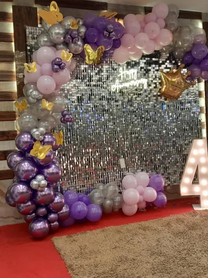 This image captures the beautiful details of the anniversary decor, from the chrome purple balloons to the delicate golden butterflies scattered throughout the arch.