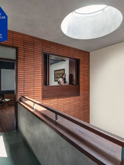 An oculus, or circular skylight, is carved into the ceiling, drawing natural light down into the circulation space. An internal window looks out from a room onto this light-filled corridor, creating layers of visual connection between different parts of the house.