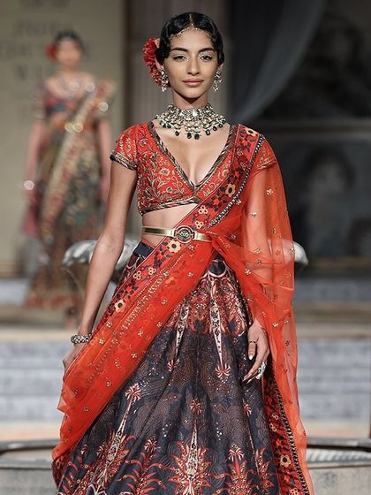 A beautiful runway look featuring a printed lehenga with a contrasting orange blouse and dupatta. We offer a blend of traditional and trendy styles for you to rent or buy.