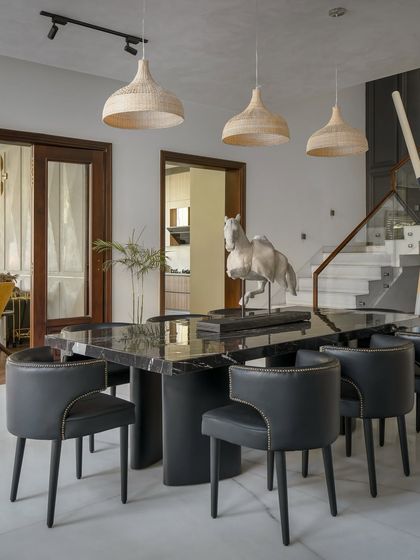 A sleek, modern dining area featuring a black marble table and sculptural horse artifact. The space is open and connected to the rest of the home, with large windows providing views of the surrounding landscape.
