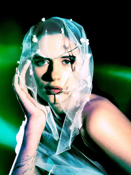 A direct and intimate portrait from 'Whispering Veil.' The model's face is framed by the pearl-studded veil, and the high-contrast green lighting adds a surreal quality.