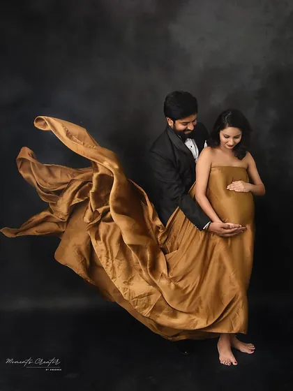 A dramatic and artistic couple's portrait. The flowing golden fabric creates a sense of motion and magic around the expecting parents.