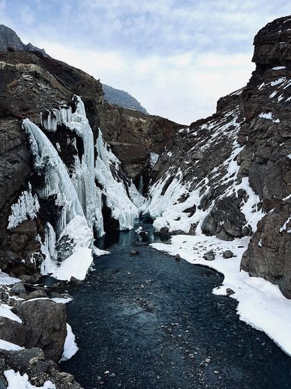 The partially frozen Lingti Waterfall in Pin Valley, a stunning display of nature's power and beauty. The contrast between the flowing water and the ice formations makes for a dramatic landscape shot.