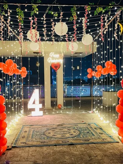 Perfect for an anniversary or birthday, this outdoor canopy decoration creates a magical evening. The setup includes a canopy draped with fairy lights, red balloon columns, and a light-up number "4" on a terrace, making for a beautiful and intimate celebration space.