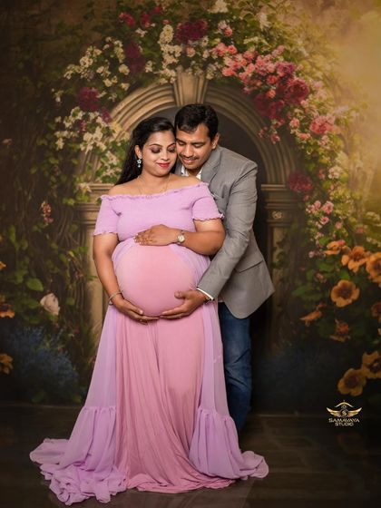 An intimate moment where the couple embraces, both cradling the baby bump. The sheer fabric of the lavender gown adds a touch of softness.