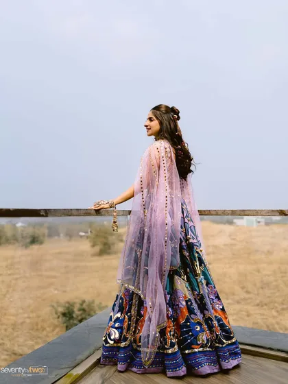 A stunning solo portrait of the bride looking out over the landscape, her unique and colorful lehenga flowing behind her.