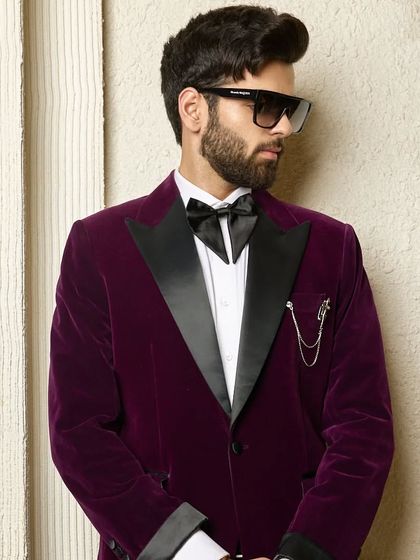 The rich texture and deep color of the wine velvet tuxedo are highlighted here. The satin lapel and accessory chain add layers of detail to this exquisite piece.