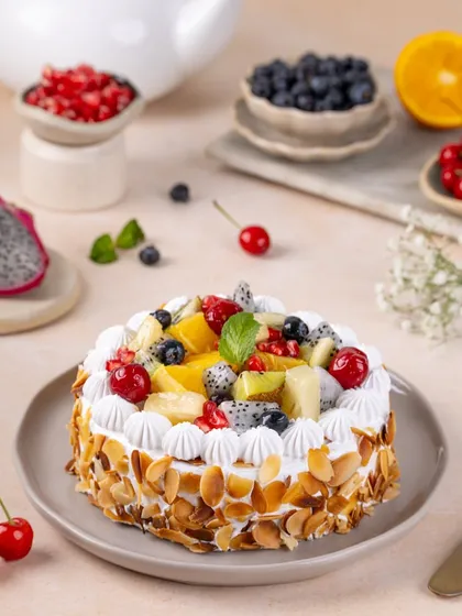 The whole fresh fruit cake, generously topped with a medley of colourful fruits and toasted almonds. This shot is bright, cheerful, and full of life.