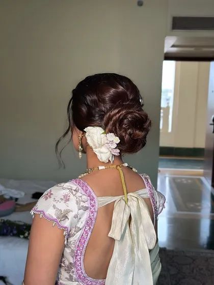 A close-up of the intricate rose bun, adorned with a fresh white flower. This is a popular and timeless choice for weddings and traditional functions.