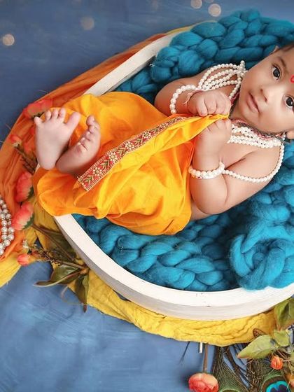 A newborn peacefully resting as little Krishna. This creative shot uses a peacock feather-inspired setup to cradle the baby, showcasing a unique take on a newborn photoshoot.