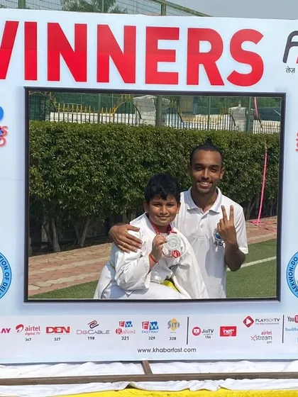 A student and coach pose in the winner's frame after a silver medal win.