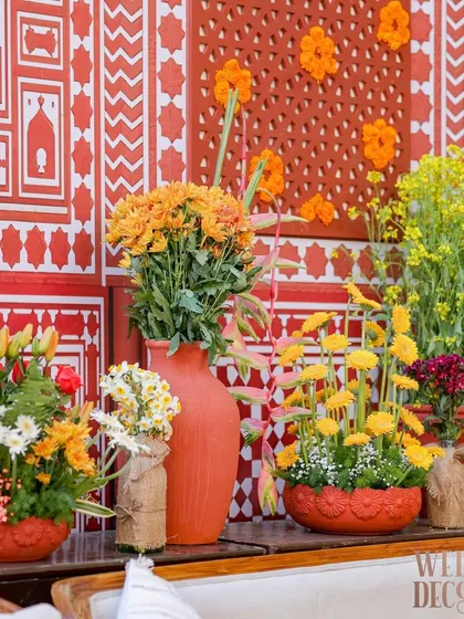 A collection of colorful floral arrangements in terracotta vases, set against the patterned wall. The mix of yellow, orange, and red flowers brought a festive energy to the space.