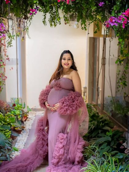 A smiling mother-to-be in a beautiful dusty rose gown, standing in one of my studio's garden-themed corners.