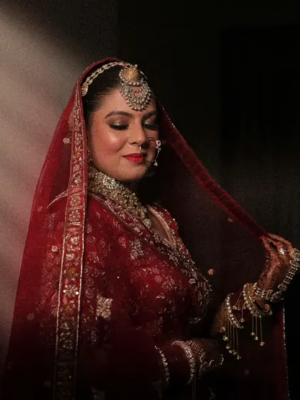 A stunning bridal portrait, with the bride's face partially illuminated, highlighting her regal jewelry and the rich color of her red attire.