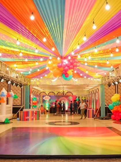 A rainbow of fun! The ceiling of this hall was transformed with vibrant, multi-colored drapes and string lights for a Trolls-themed birthday party, creating a festive canopy over the entire celebration.