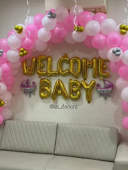 For a simple and sweet welcome, I can create a beautiful balloon arch right above your sofa. This design uses pink and white balloons with gold 'WELCOME BABY' letters, instantly making your living room feel festive.