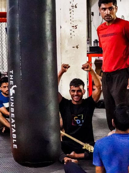 A moment of victory and encouragement during a group session. A coach looks on as a member celebrates after completing a tough drill on the heavy bag. This is the supportive atmosphere we cultivate.