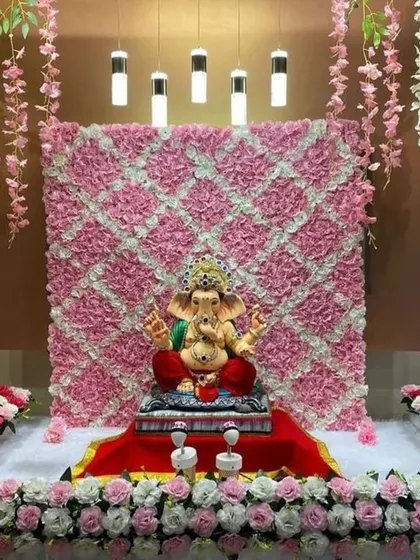 A chic and modern Ganpati decor with a quilted pink floral backdrop. The design is framed by hanging wisteria and a base of pink and white roses, creating a stylish and textured look.