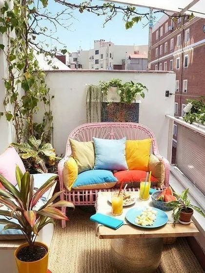 A concept for a bright and cheerful balcony, using colorful cushions on wicker furniture and plenty of potted plants to create a vibrant, cozy corner for relaxing.