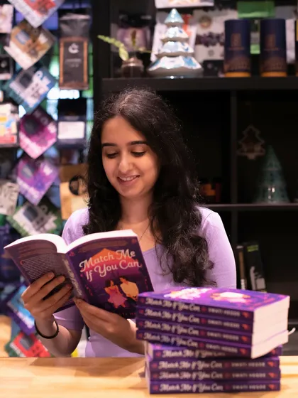 Reading a copy of *Match Me If You Can* in a cafe. This book is set in Mumbai and is filled with delicious food descriptions and a whole lot of heart.