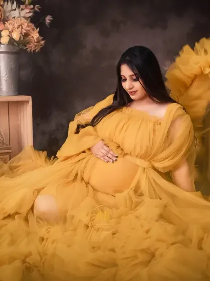 A serene seated portrait in a vibrant yellow ruffled gown. The fabric is spread out beautifully, surrounded by rustic props and floral arrangements for a complete artistic setup.