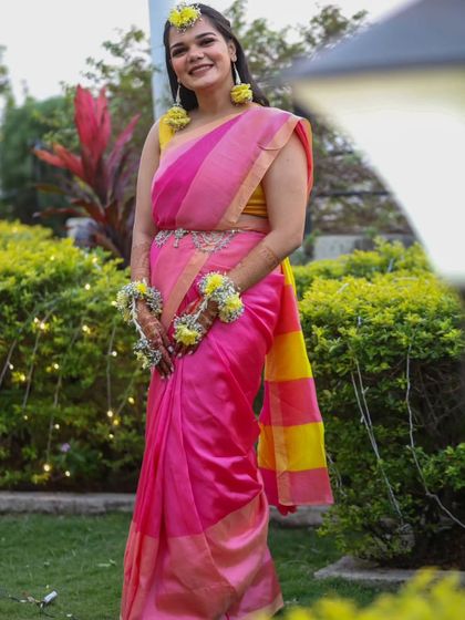 A full-length outdoor shot of the saree Haldi look, showing how the bright colors pop against the green background.