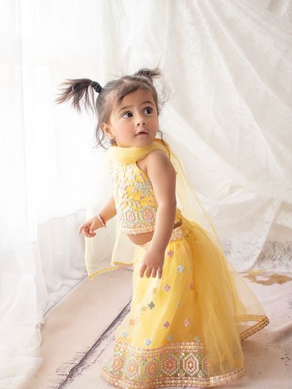 A precious moment captured of this little girl in a traditional yellow lehenga. Her curious expression and pigtails are just too cute.