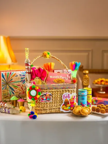 An elegant wicker basket Holi hamper, filled with gujiyas, mathri, and other festive snacks.
