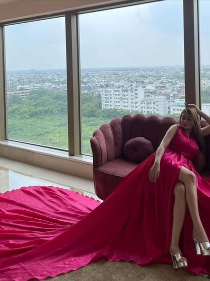 A client lounging on a sofa by a large window, with the long train of her pink satin gown spread out, creating a luxurious and relaxed look.
