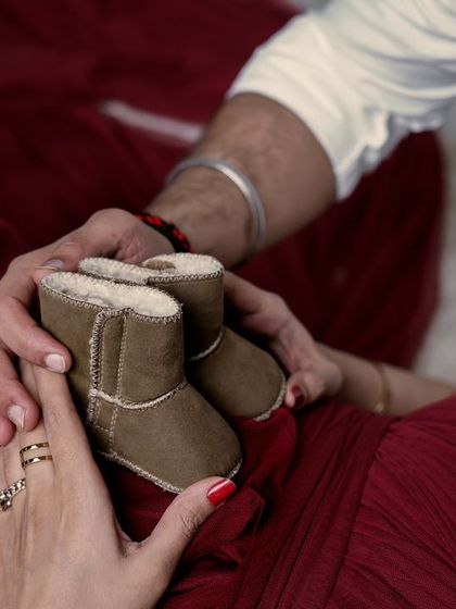A close-up detail of an expecting couple holding a pair of tiny boots over the baby bump. These prop shots add a sweet and symbolic touch to your maternity photoshoot.