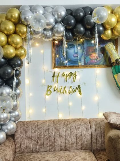 A simple yet elegant home birthday setup with a gold, black, and silver balloon arch, fairy lights, and a champagne bottle foil balloon.