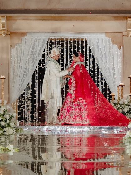 The varmala exchange, a pivotal moment in the ceremony, set against a backdrop of shimmering floral curtains.