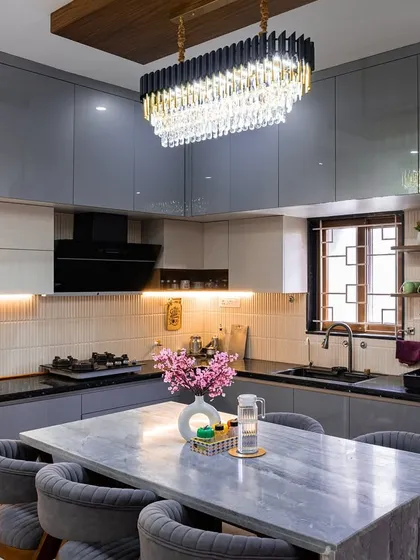 This is a modern kitchen designed for both cooking and conversation. It features sleek grey cabinetry, a stunning chandelier, and a marble-topped island that doubles as a dining space, making it the true heart of the home.