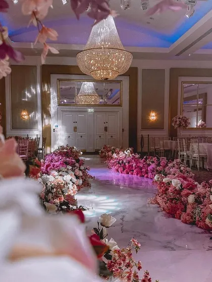 I can create a magical entrance for the bride. This walkway is lined with beautiful pink and white flower arrangements on the floor, leading to a grand hall.