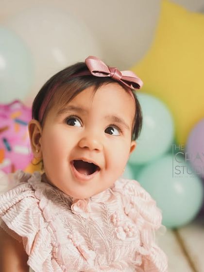 A close-up of pure first-birthday excitement. Her mouth is open in a happy shout, surrounded by fun donut and star balloons.