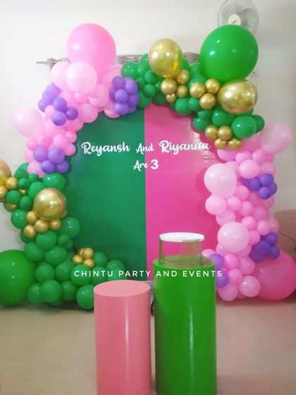 A simple and colorful decoration for a twins' birthday party. The split-color backdrop in green and pink is framed by a matching balloon garland.