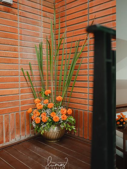 A beautiful corner arrangement with marigolds in a brass pot against a brick wall.